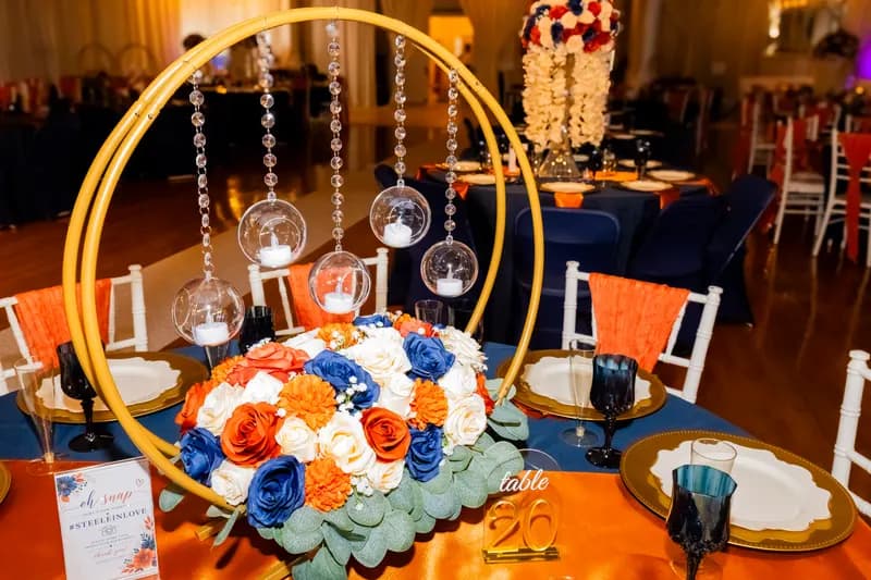 Wedding centerpiece: gold hoop with hanging candles over orange, navy and white roses