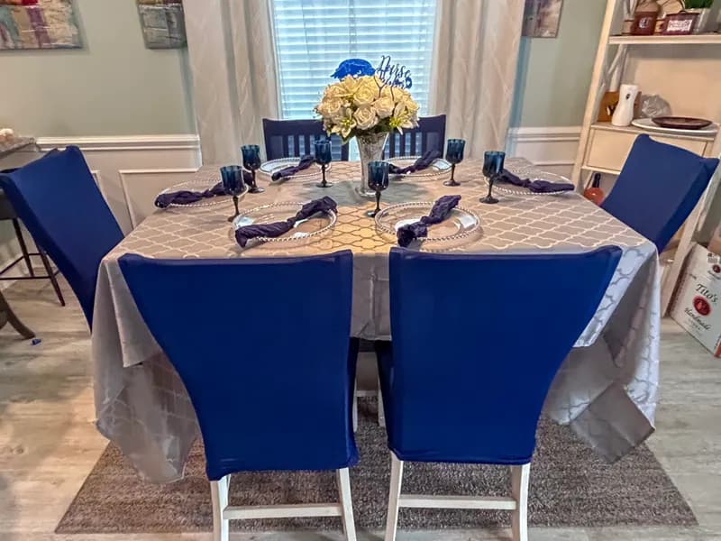 Intimate dinner table with navy chair covers, silver linens and a white floral centerpiece
