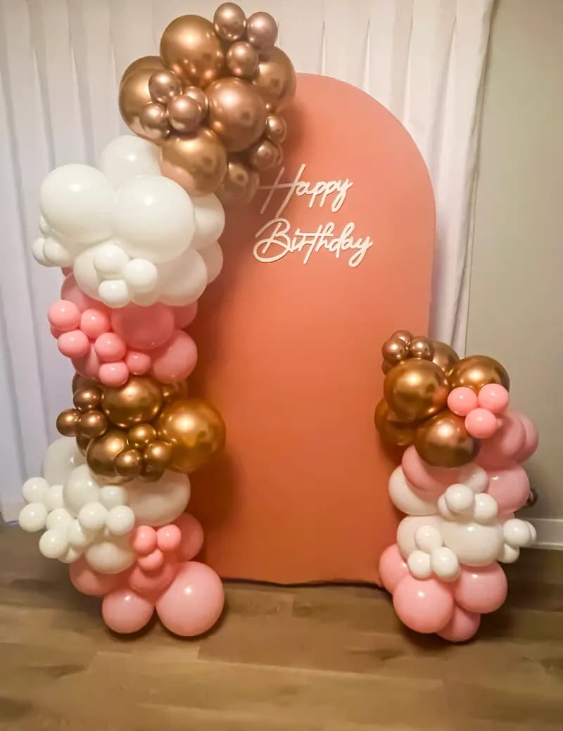 Terracotta arch backdrop with a 'Happy Birthday' script sign, framed by pink, white and chrome gold balloon garlands