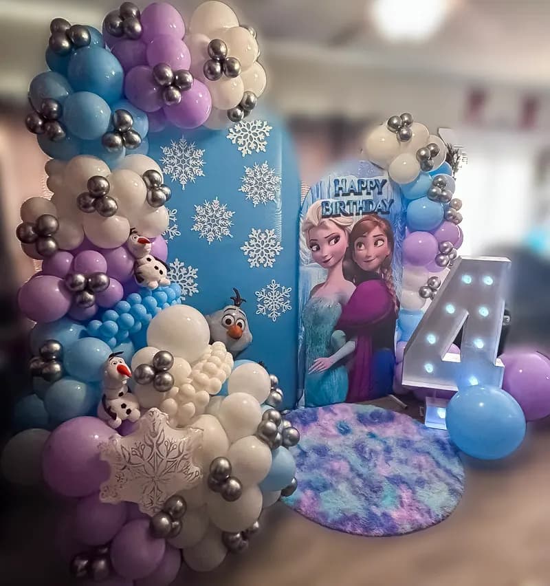 Frozen-themed fourth birthday with snowflake backdrop and blue, lilac and silver balloons