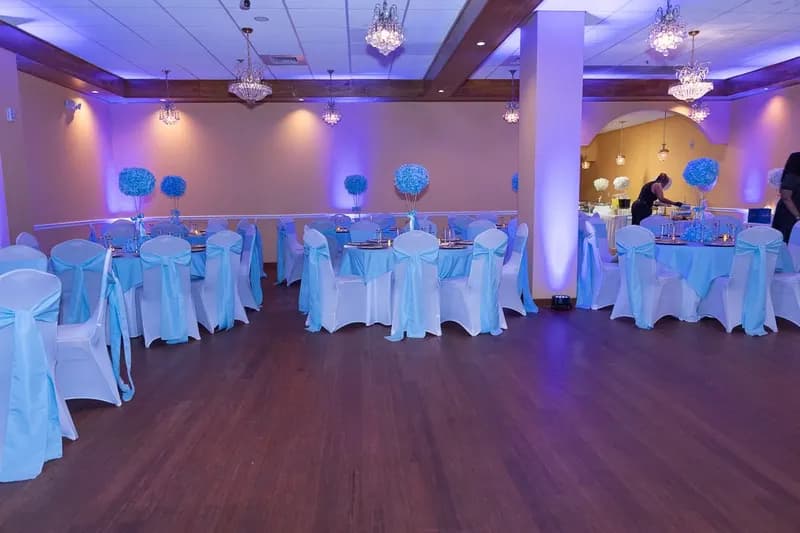 Ballroom with white chair covers, turquoise sashes and blue uplighting